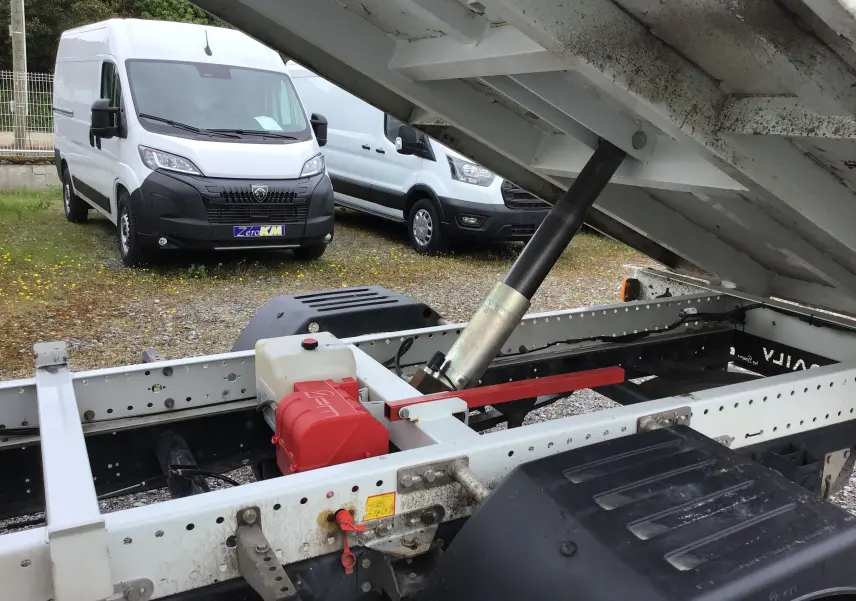 Vue avant gauche d'un utilitaire Iveco Daily blanc avec benne relevée et coffre visible sur châssis apparent.