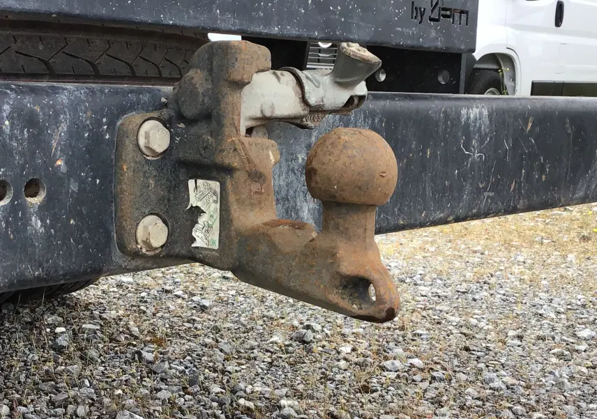 Gros plan sur l'attelage rouillé à l'arrière d'un Iveco Daily Chassis double cabine blanc, avec benne et coffre visible en arrière-plan.