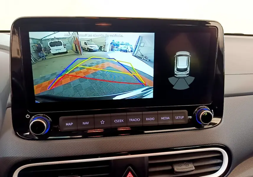 Écran tactile central du Hyundai Kona noir 2020 montrant l'aide au stationnement arrière avec caméra et capteurs.