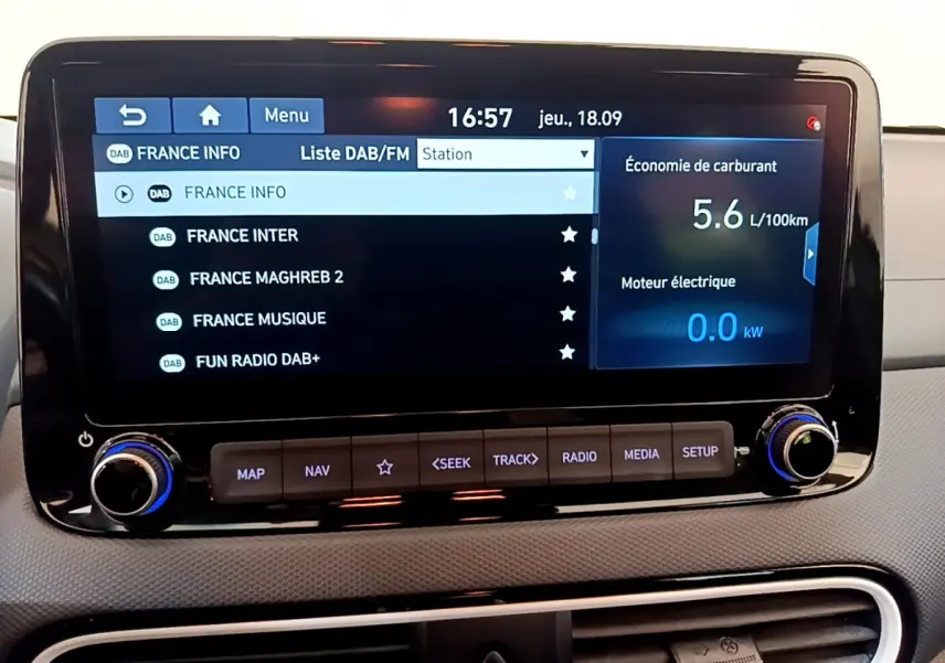 Écran tactile central du tableau de bord du Hyundai Kona noir, affichant la liste des radios DAB et consommation hybride.