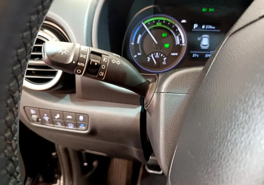 Gros plan sur la manette de feux à gauche du volant cuir du Hyundai Kona hybride noir, avec tableau de bord numérique en arrière-plan.