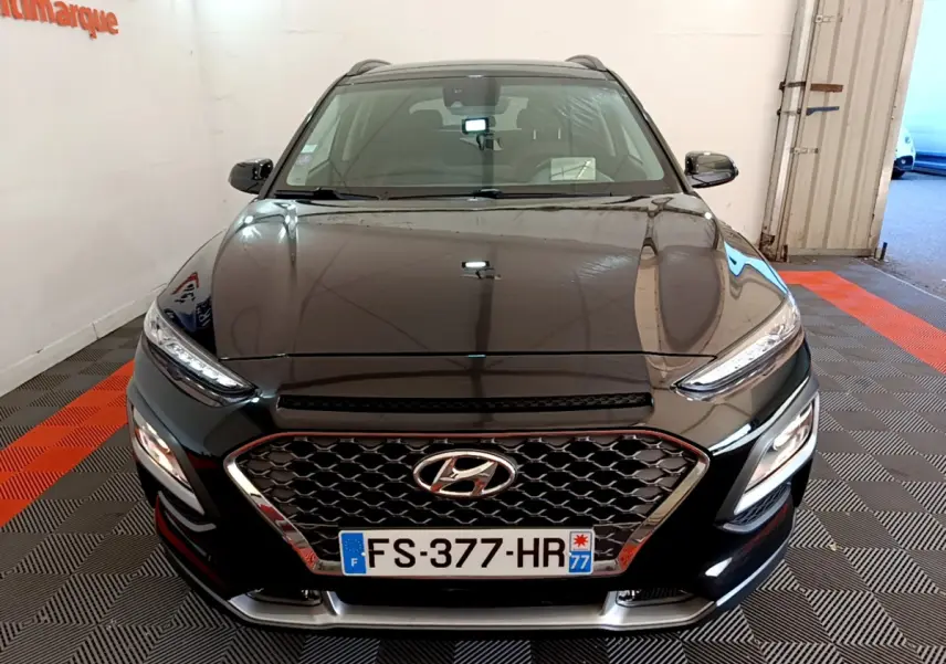 Vue avant d'un Hyundai Kona noir 2020 avec calandre hexagonale et feux LED, stationné en intérieur sur sol à motifs.