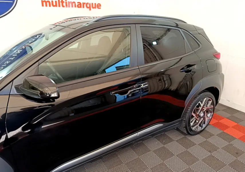 Vue latérale côté gauche d'un Hyundai Kona noir brillant avec jantes alliage et rétroviseurs noirs dans un showroom.