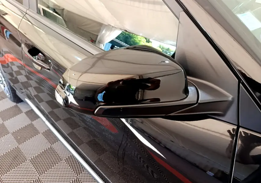 Rétroviseur noir côté gauche du Hyundai Kona 2020 hybride, avec porte et poignée visibles en reflet.