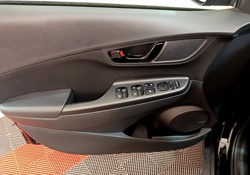 Vue rapprochée de la porte avant gauche noire du Hyundai Kona 1.6 GDi Hybrid avec commandes électriques et haut-parleur Bose.