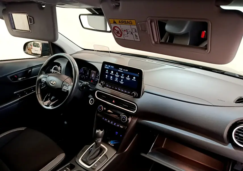 Vue intérieure côté conducteur du tableau de bord noir du Hyundai Kona 1.6 GDi Hybrid avec écran tactile central et volant multifonctions.