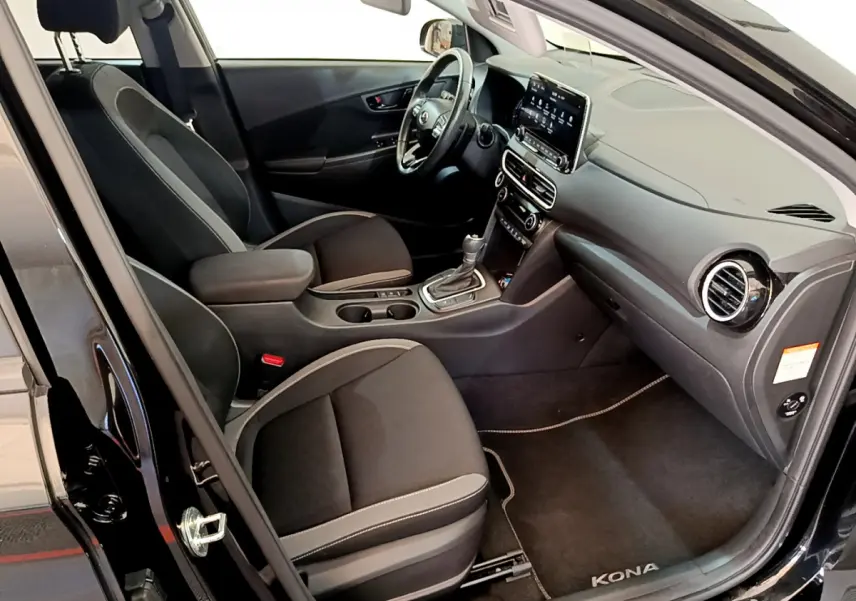 Intérieur côté conducteur d'une Hyundai Kona noire, montrant sièges noirs, volant cuir et écran tactile central.
