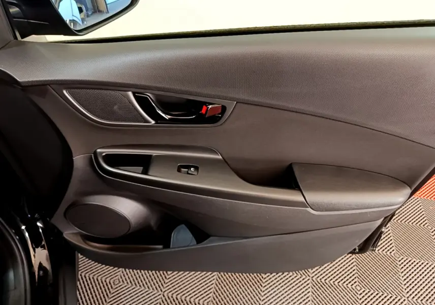 Intérieur côté gauche de la porte avant d'un Hyundai Kona noir, avec poignée chromée et commande de vitre électrique.