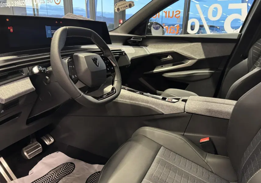 Intérieur avant droit du Peugeot 3008 Hybrid 2025, avec volant compact, sellerie tissu gris et décor tissu Rimini chiné.