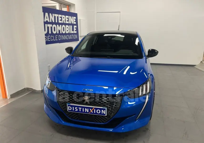 Peugeot 208 bleu en 3/4 avant, avec calandre noire distinctive et phares LED, vue dans un showroom intérieur.