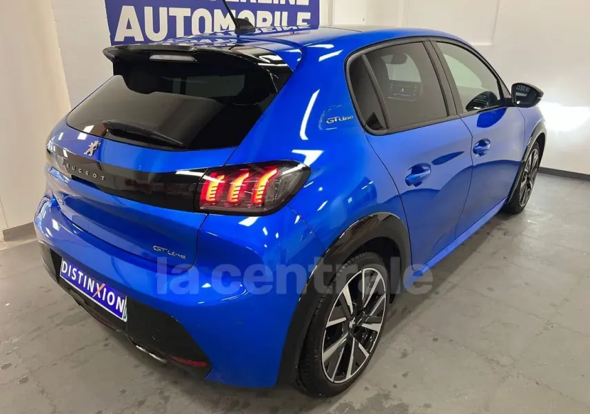 Vue 3/4 arrière droite d'une Peugeot 208 GT Line bleue de 2020 avec feux arrière allumés et jantes alliage noires.