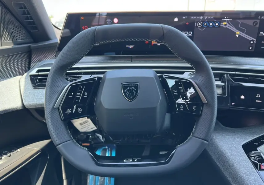 Vue intérieure centrée sur le volant GT du Peugeot 3008 Hybrid 2025 avec tableau de bord numérique et finitions grises.