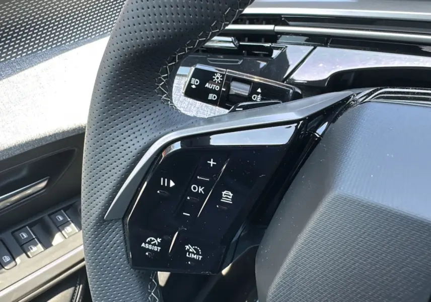 Gros plan sur les commandes au volant du Peugeot 3008 hybride 2025 avec finition noire brillante et cuir perforé.