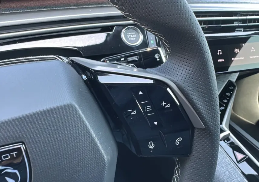 Gros plan sur le volant perforé du Peugeot 3008 Hybrid 2025 avec commandes intégrées et bouton démarrage visible.