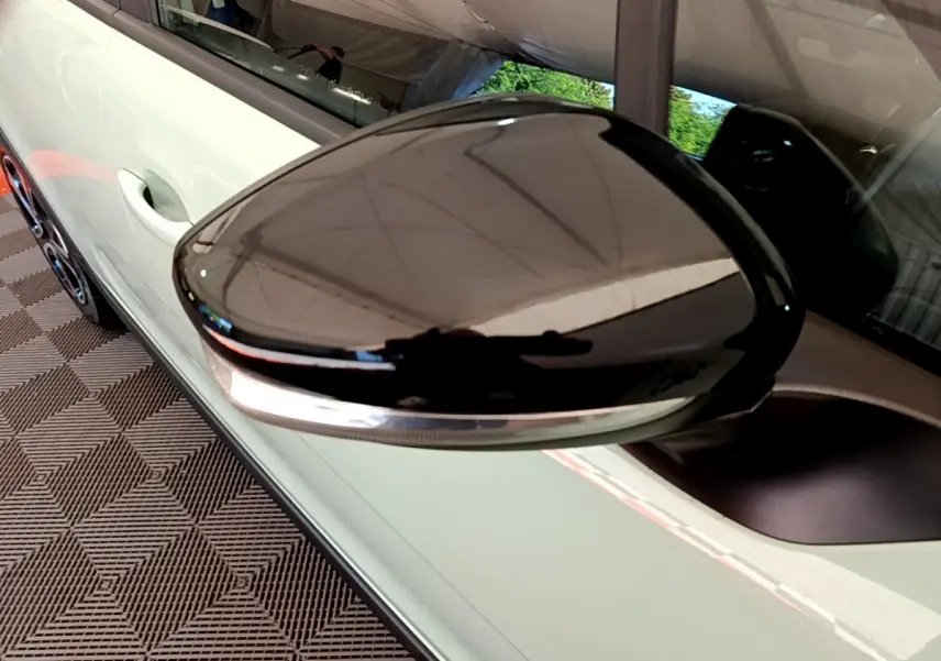 Gros plan sur le rétroviseur noir brillant côté gauche d'une Citroën C3 vert clair, avec poignée de porte visible.
