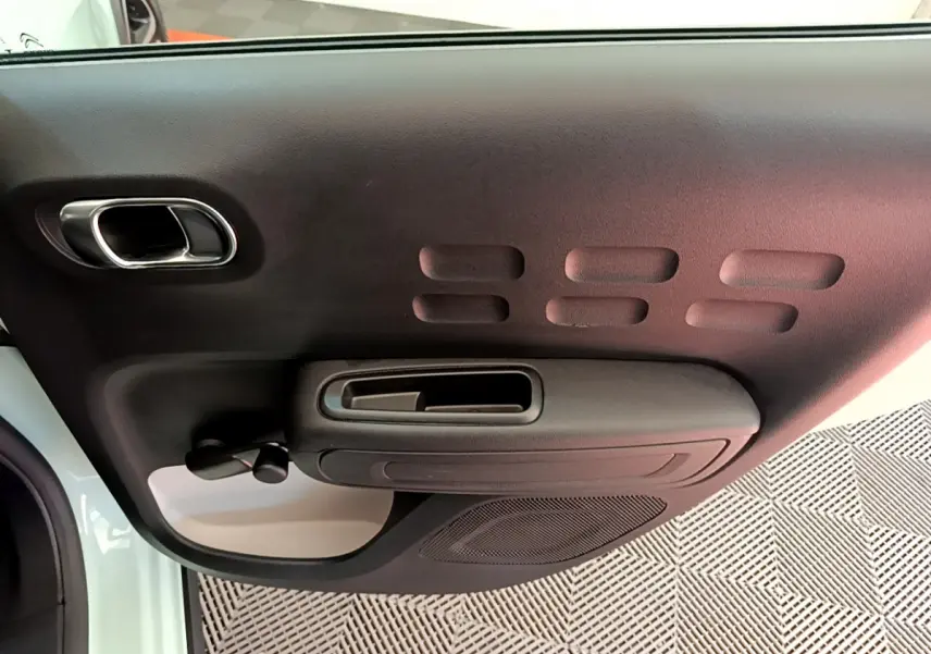 Vue rapprochée de la porte intérieure côté gauche de la Citroën C3 PureTech 82 verte avec poignée et commande de vitre manuelle.