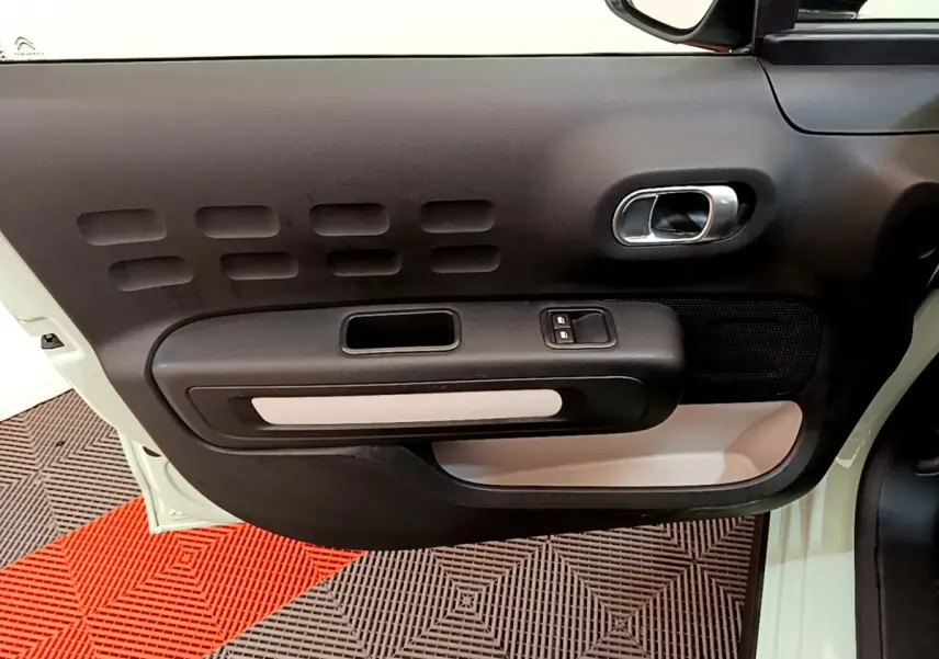 Intérieur côté gauche de la porte avant d'une Citroën C3 vert clair, avec poignée argentée et commandes de vitres.