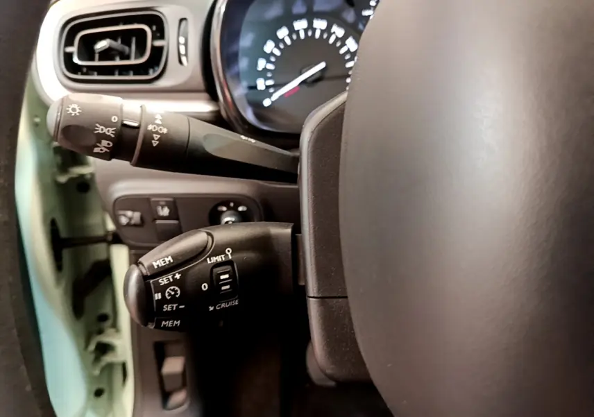 Gros plan sur la commande de régulateur de vitesse et le commodo d’éclairage dans une Citroën C3 vert 2019.