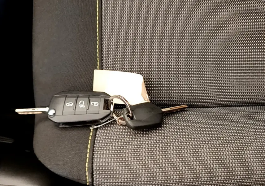 Clé de voiture Citroën C3 PureTech posée sur siège tissu gris avec surpiqûres vertes, vue rapprochée intérieure.