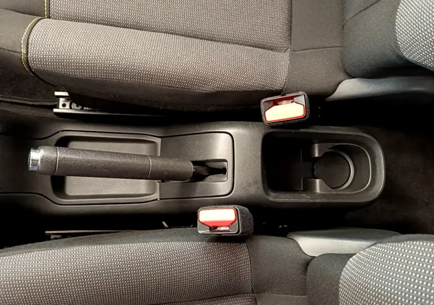 Vue plongeante sur la console centrale noire avec frein à main et ceintures rouges entre les sièges tissu gris de la Citroën C3.