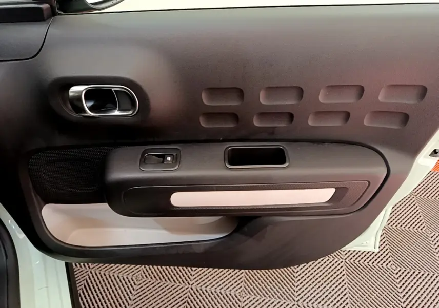 Gros plan sur la porte côté gauche vert clair de la Citroën C3 avec poignée chromée et bouton de commande de vitre.