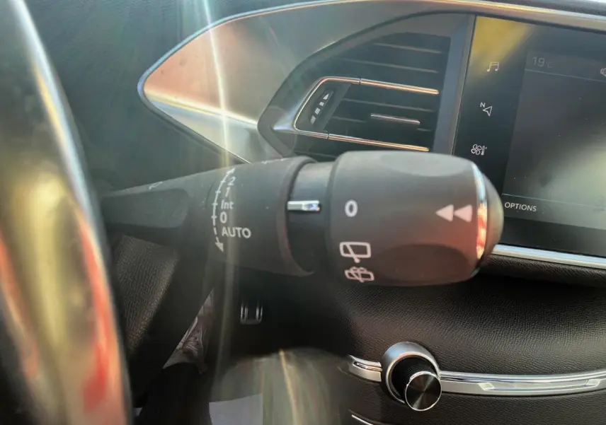 Gros plan sur la commande d'essuie-glace à gauche du volant dans l'habitacle noir d'une Peugeot 308 SW gris clair.