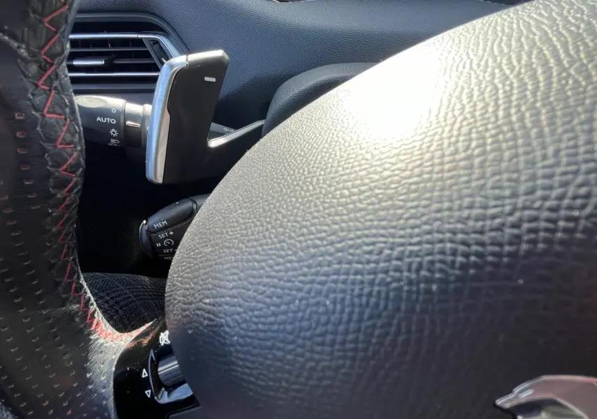 Gros plan sur le volant noir à surpiqûres rouges de la Peugeot 308 SW GT Line, mettant en valeur la commande au volant.