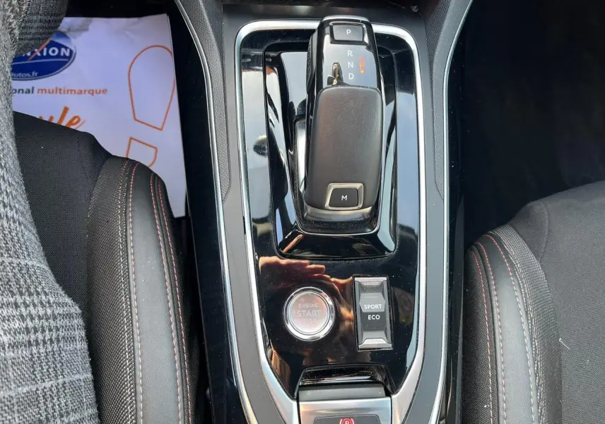 Vue plongeante sur la console centrale noire brillante de la Peugeot 308 SW GT Line, avec levier de vitesse auto et bouton start/stop.