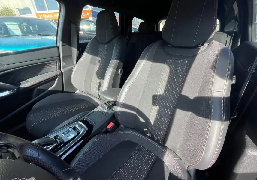 Vue intérieure côté avant droit des sièges en tissu noir avec surpiqûres rouges et console centrale d'une Peugeot 308 SW gris clair.