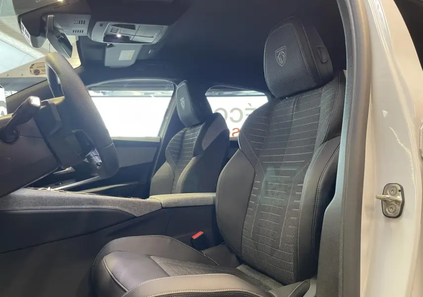 Vue intérieure côté conducteur du Peugeot 3008 blanc Okenite, sièges sport noirs avec logo Peugeot brodé sur appuie-tête.