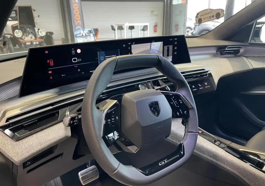 Vue intérieure du volant compact GT et du tableau de bord numérique du Peugeot 3008 Hybrid blanc Okenite.
