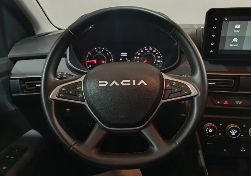 Vue rapprochée du volant en cuir noir de la Dacia Sandero 2024 avec commandes multifonctions et tableau de bord digital.