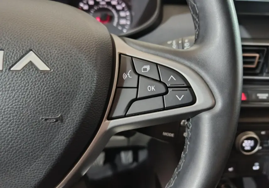 Gros plan sur le volant cuir noir de la Dacia Sandero 2024 avec commandes multifonctions et tableau de bord en arrière-plan.