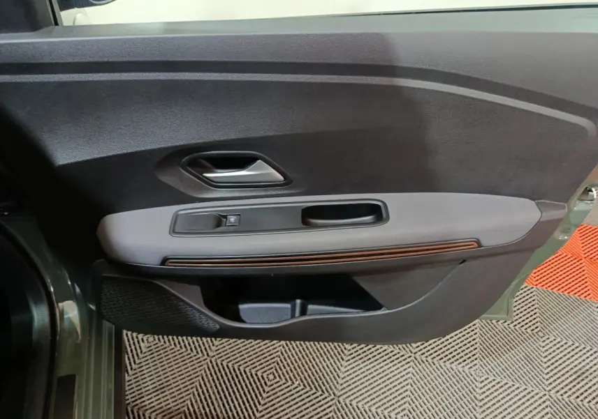 Vue intérieure côté gauche de la porte avant d’une Dacia Sandero Extreme+ TCe 110 2024 verte, avec poignée argentée et commande de vitre.