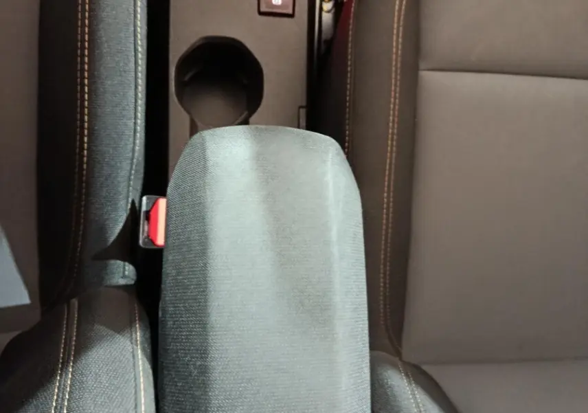 Vue plongeante sur l'accoudoir central et les sièges avant gris avec surpiqûres orange de la Dacia Sandero 2024.