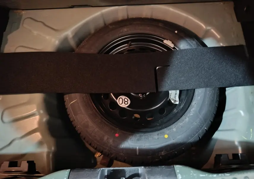 Vue rapprochée de la roue de secours galette noire dans le coffre vert de la Dacia Sandero Extreme+ TCe 110 2024.