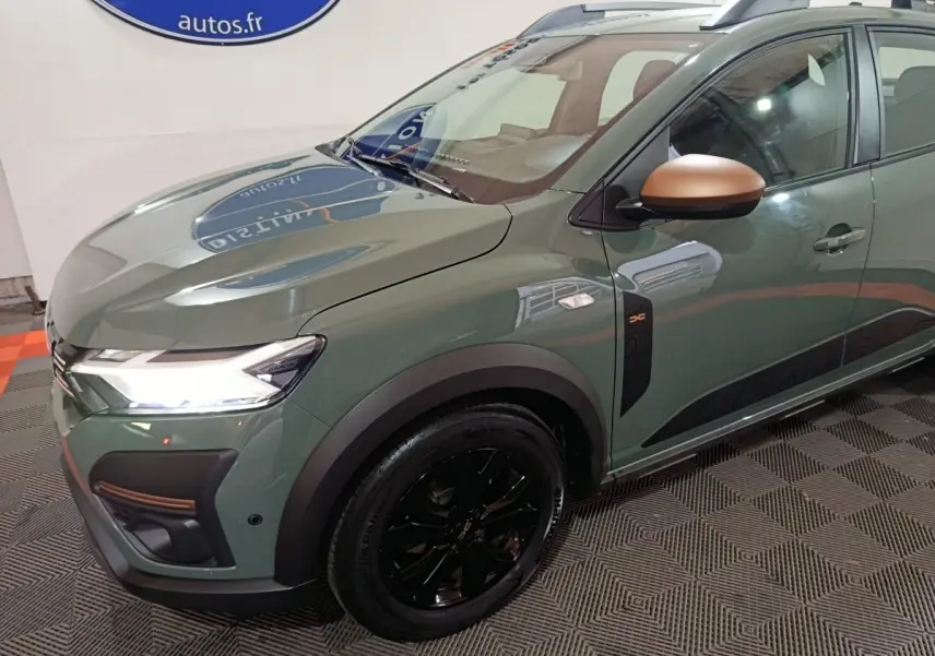 Vue 3/4 avant droit d'une Dacia Sandero Extreme+ 2024 vert avec rétroviseurs cuivrés et jantes noires brillantes.