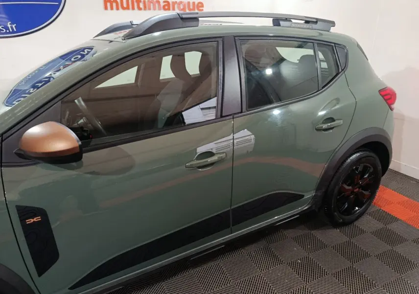 Vue latérale gauche d'une Dacia Sandero Extreme+ 2024 vert avec rétroviseur cuivré et jantes noires distinctives.