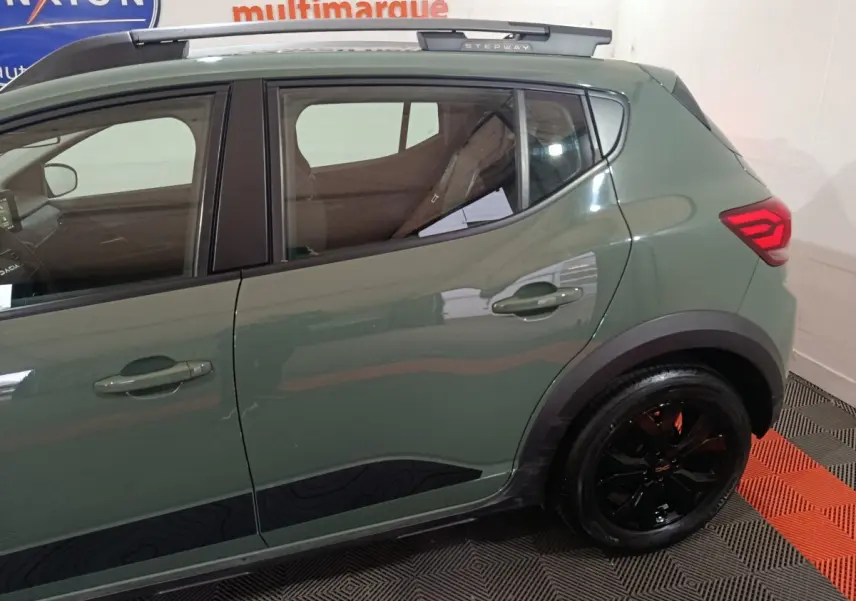 Vue latérale droite d'une Dacia Sandero Extreme+ TCe 110 2024 verte avec jantes noires et rails de toit assortis.