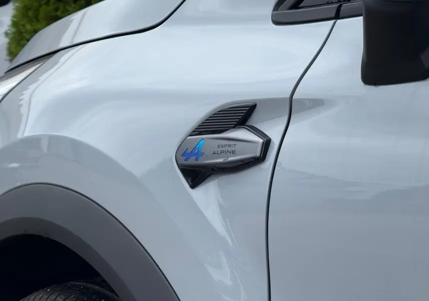 Gros plan sur l'aile avant gauche grise Rafale du Renault Symbioz 2026 avec logo Esprit Alpine bleu et noir.
