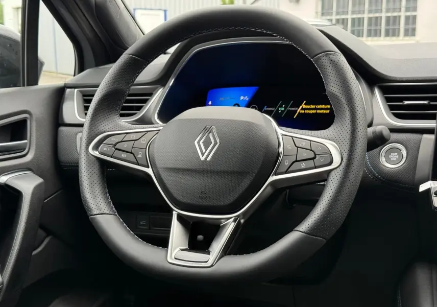 Vue rapprochée du volant noir perforé de la Renault Symbioz 2026 avec tableau de bord digital et bouton Start/Stop.