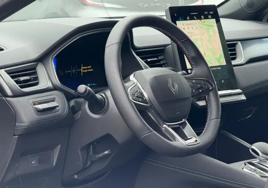 Vue intérieure côté conducteur du Renault Symbioz gris Rafale, volant multifonction et écran tactile vertical avec navigation.