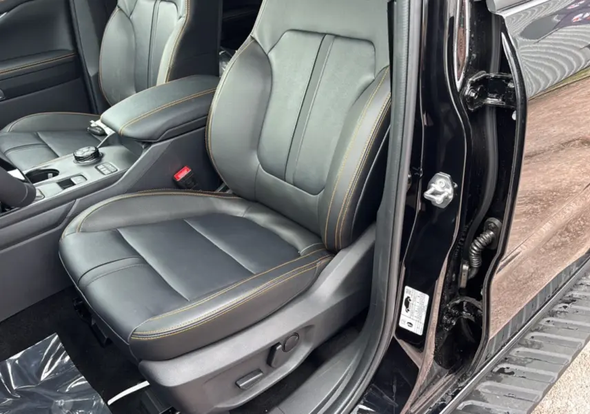 Vue intérieure côté conducteur du Ford Ranger 2025 noir agate, siège en cuir noir avec surpiqûres orange et console centrale visible.