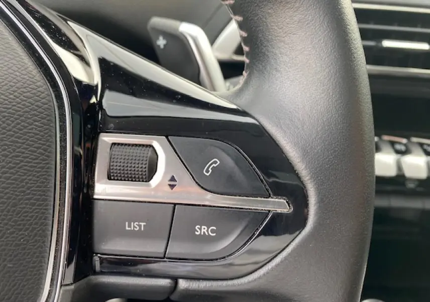 Gros plan sur les commandes gauche du volant cuir noir du Peugeot 3008 gris platinium 2021 finition Allure Pack.