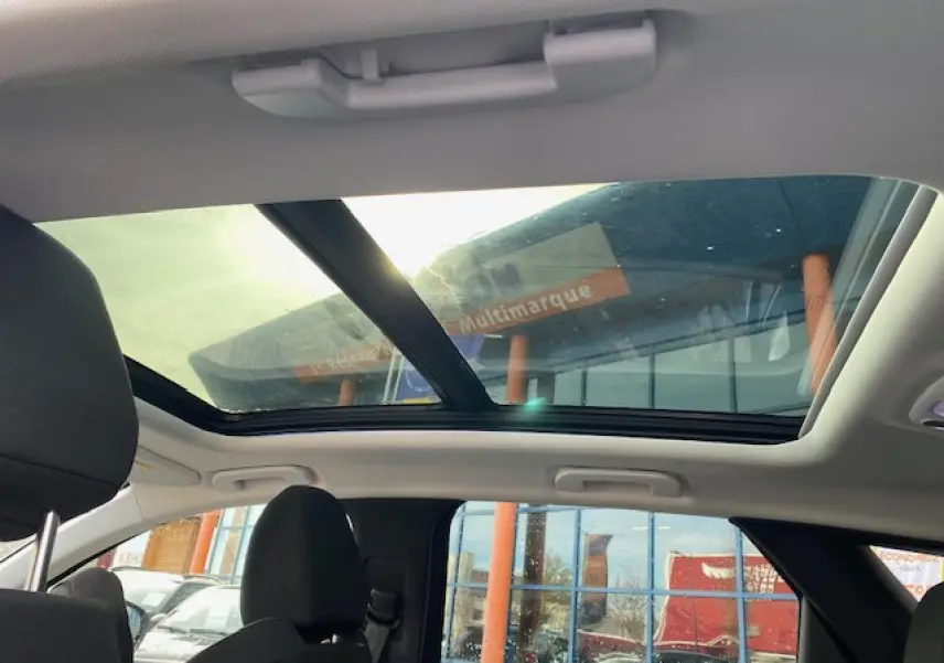 Toit ouvrant panoramique vu de l'intérieur arrière du Peugeot 3008 gris platinium avec sièges noirs et ciel de toit clair.