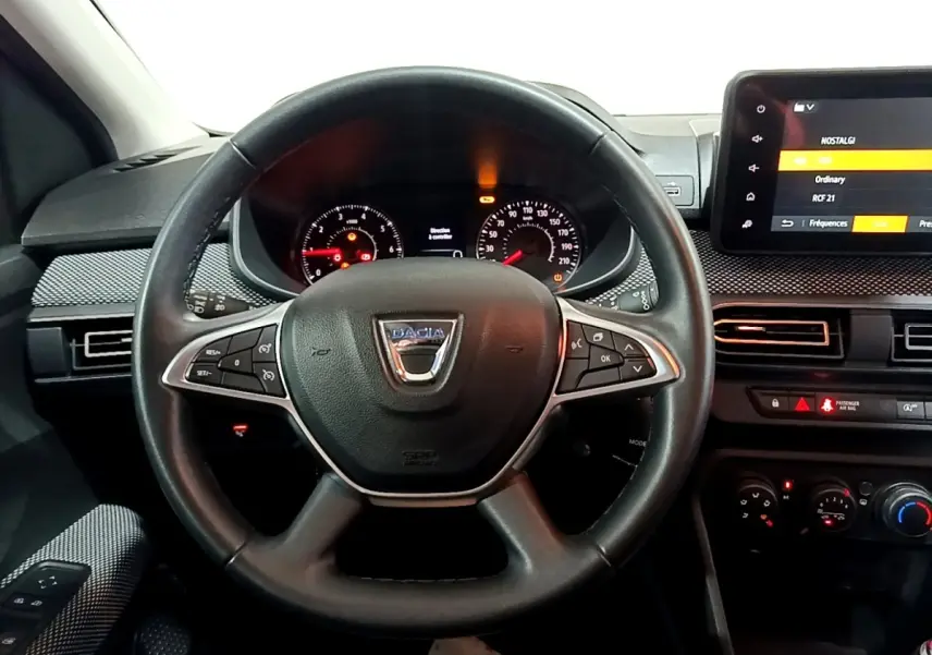 Vue intérieure centrée sur le volant cuir noir multifonctions de la Dacia Sandero blanc, avec tableau de bord et écran tactile.