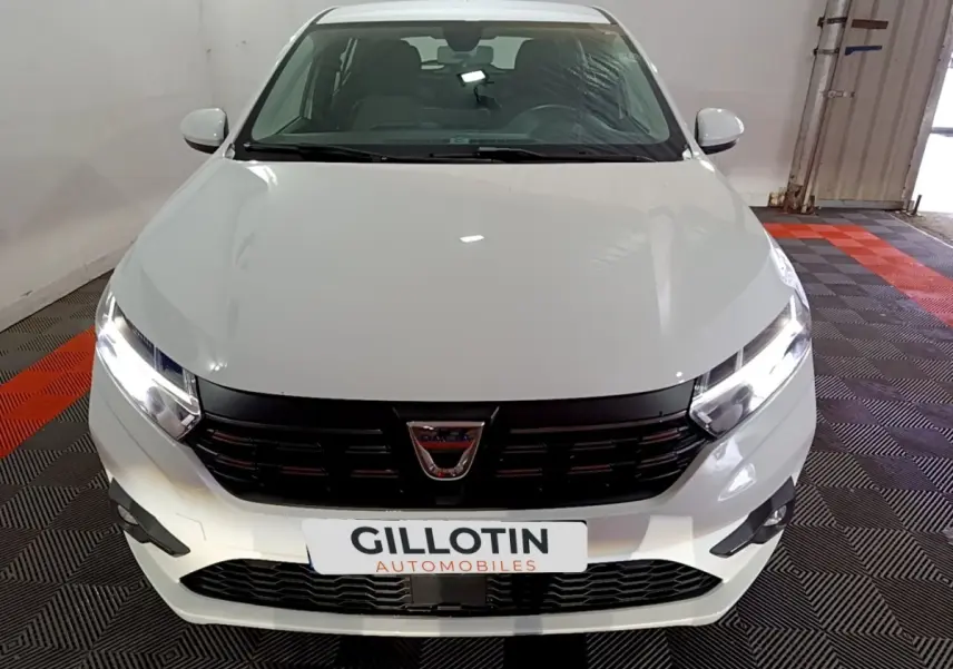 Vue frontale d'une Dacia Sandero blanche 2022 avec phares LED allumés et calandre noire brillante.