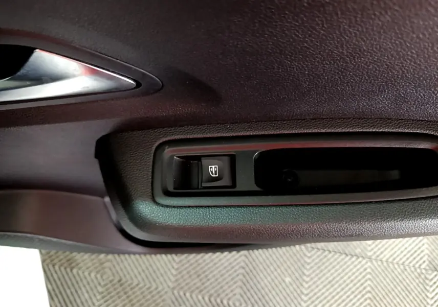 Gros plan sur le bouton de commande de la vitre électrique sur la porte intérieure noire d'une Dacia Sandero blanche.