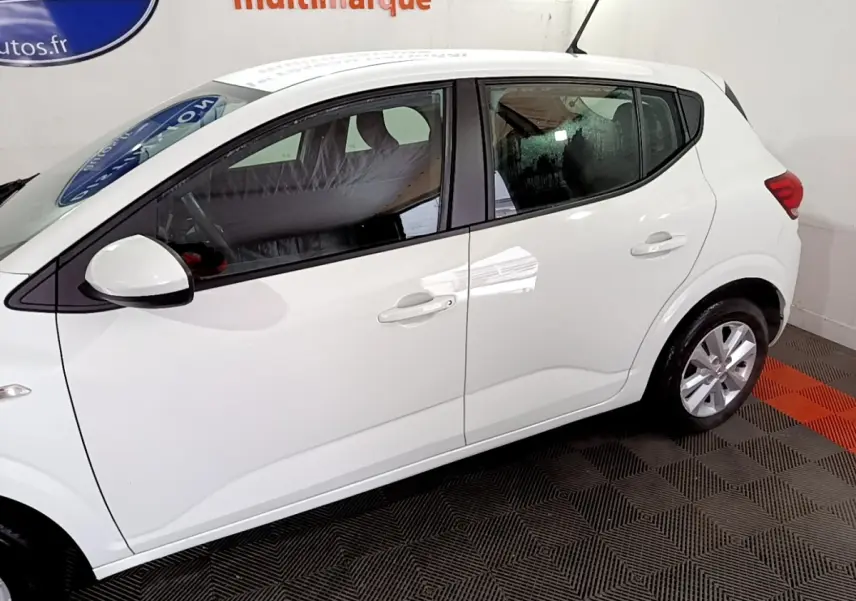 Vue de profil côté gauche d'une Dacia Sandero blanche 2022, avec poignées de porte et rétroviseur assortis.