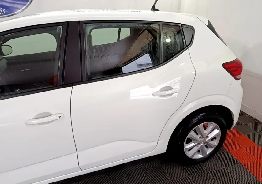 Vue latérale côté droit d'une Dacia Sandero blanche 2022, mettant en valeur les portes arrière et la roue arrière.